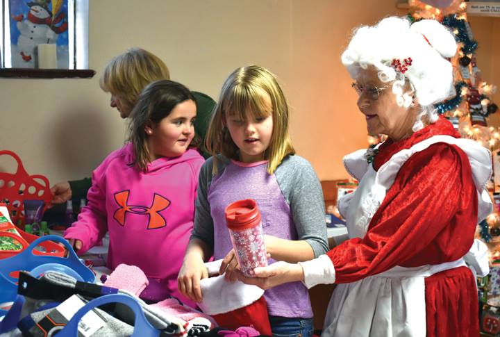 Photo in Mountain Mail Newspaper of kids with Mrs Claus helping select a gift for their parents or guardians in the kids corner