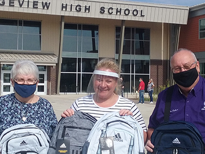 Elks in face masks hold up backpacks from their Gratitude Grant program.