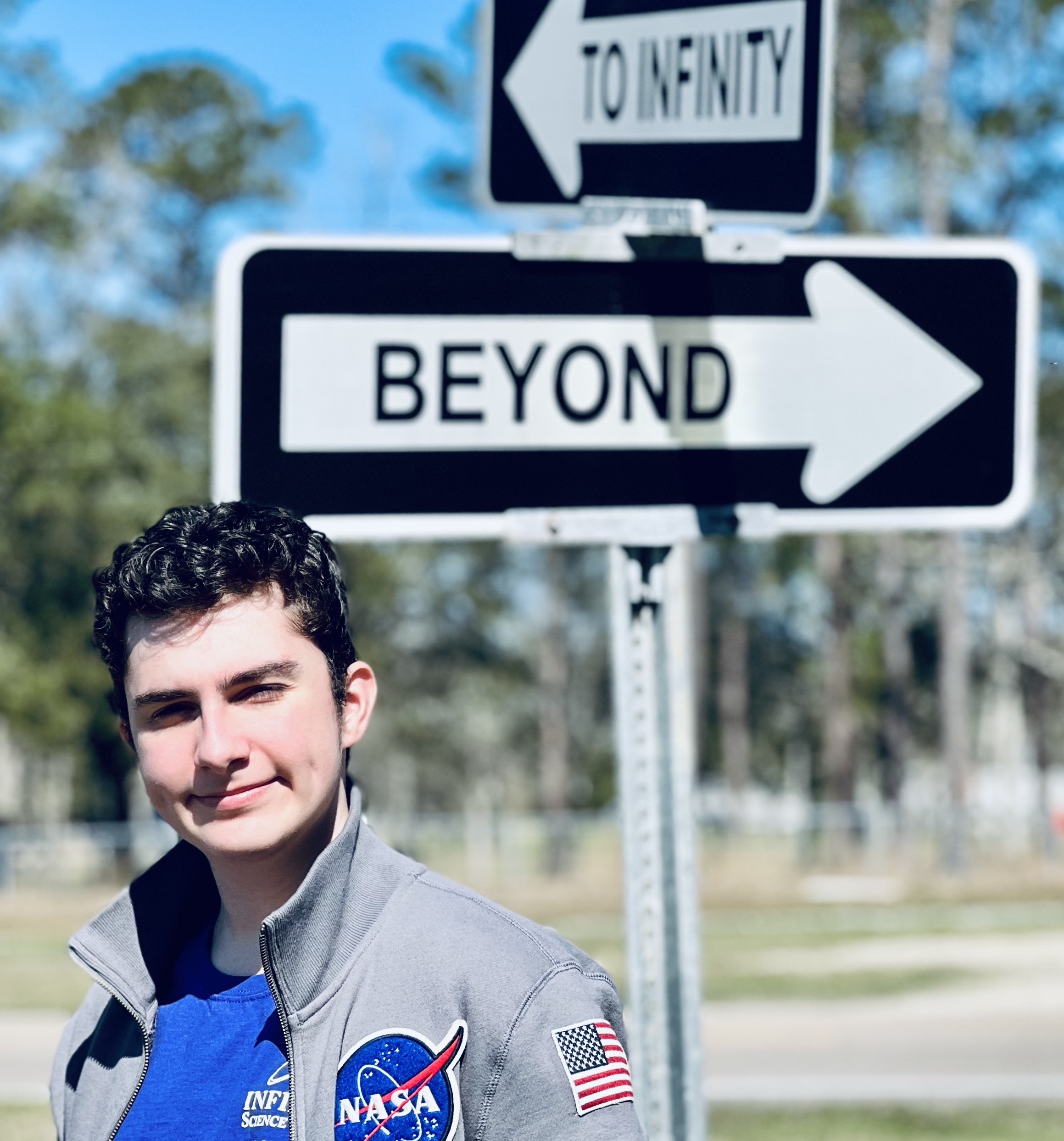 Kaden Oqueli-White stands in front of a street sign that says to infinity and beyond