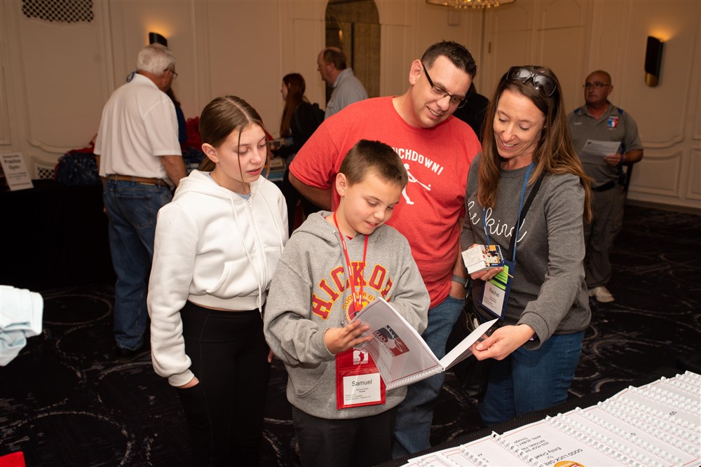 Samuel Nolan holds his trading card binder while his sister, dad and mom stand behind him and smile