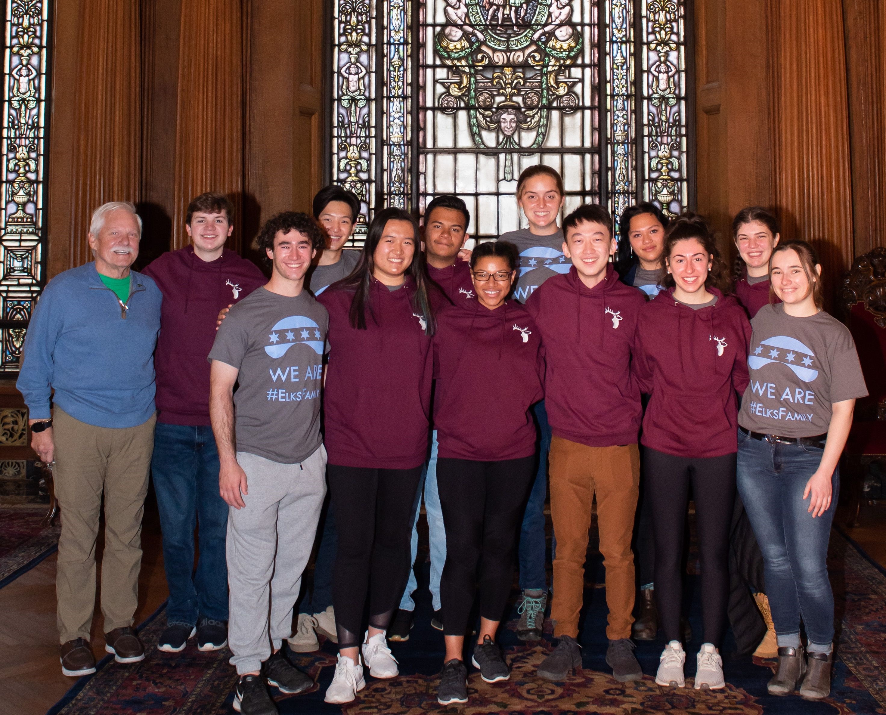 a group of Elks scholars in Elks scholar sweatshirts and Chicago Service Trip t-shirts pose for a photo in front of ornate stained glass window
